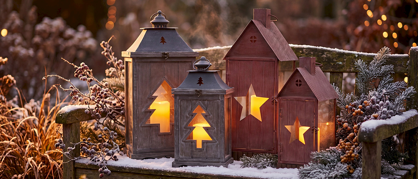 Sujets de No&euml;l en r&eacute;sine et veilleuses lumineuses en porcelaine &agrave; motifs de sapins et d&rsquo;&eacute;toiles, pos&eacute;es dans la neige devant une fen&ecirc;tre givr&eacute;e.